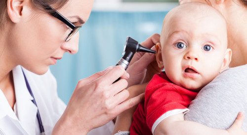 Young doctor examining baby boy with otoscope